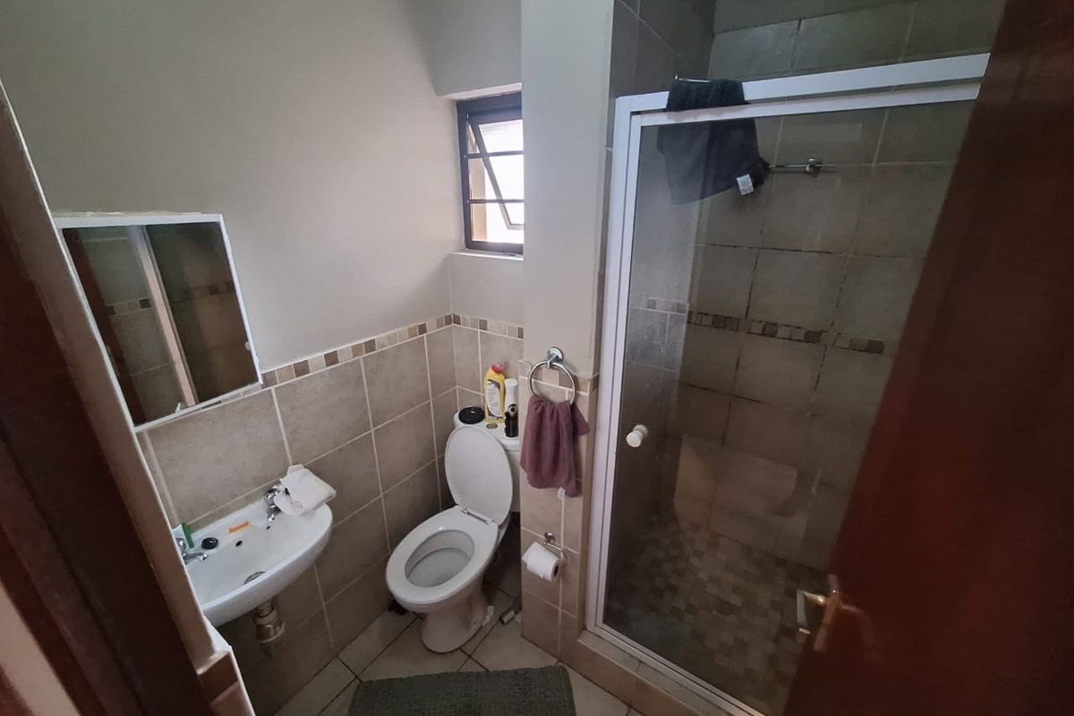 A compact bathroom featuring a shower enclosure, wall-mounted basin, and toilet with neutral tiled finishes.
