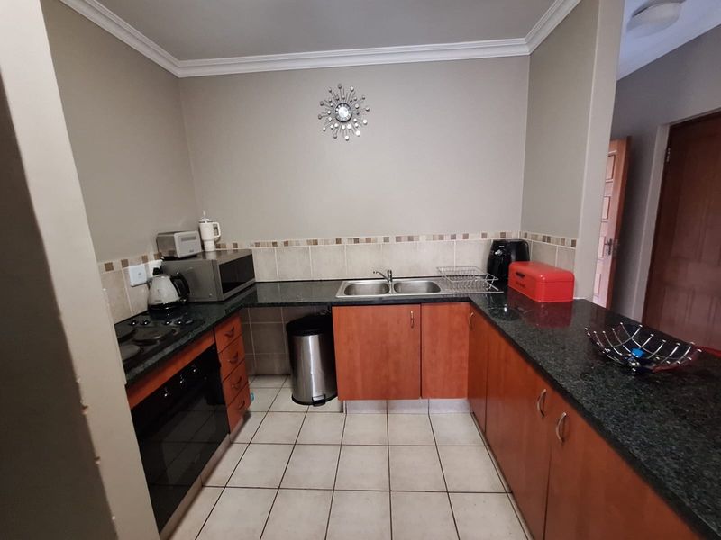 Functional kitchen featuring granite countertops, built-in oven, electric hob, double sink, and ample laminate cabinetry with tiled flooring.