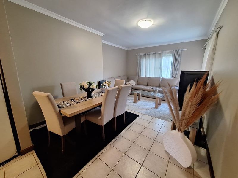 An open-plan living and dining area featuring neutral wall tones, ceramic tiled flooring, and decorative ceiling cornices.