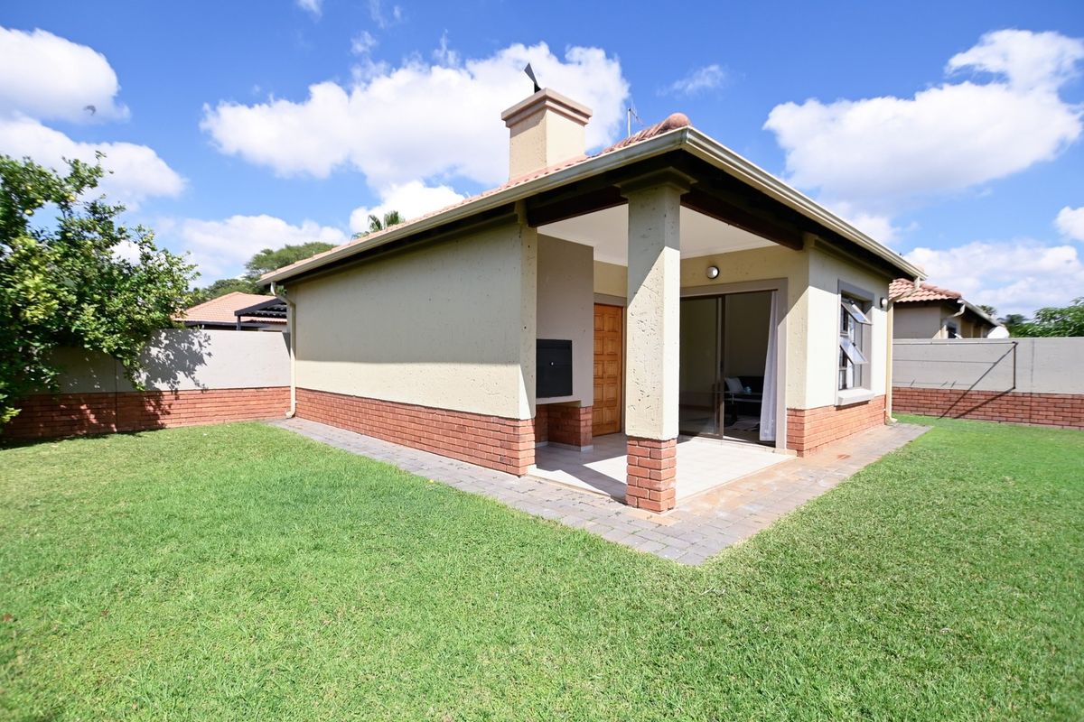 Rear view of the townhouse featuring a covered patio with a built-in braai, brick exterior accents, and a private garden area.