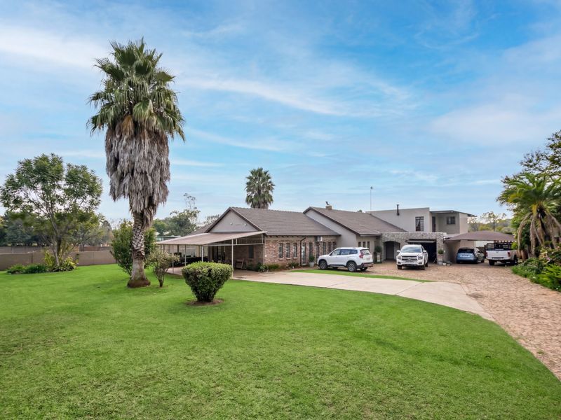 Spacious front exterior view of the house featuring a large manicured lawn, concrete driveway, covered patio area, and integrated carport parking.