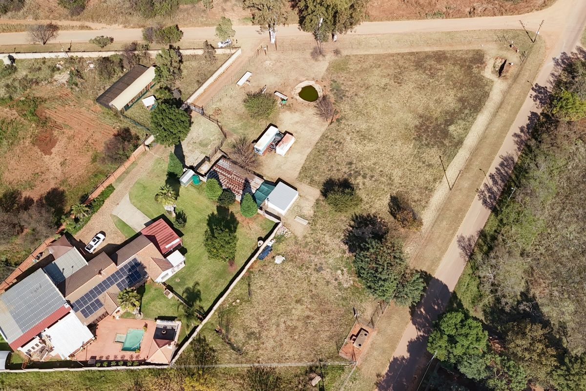 Aerial view of the property showing the main dwelling with solar panels, a swimming pool, outbuildings, and expansive grounds within a fenced perimeter.