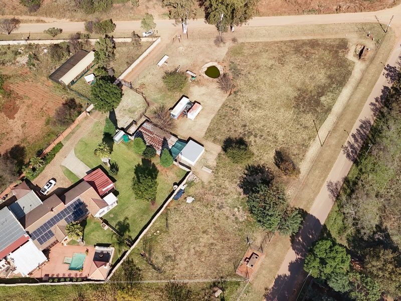 Aerial view of the property showing the main dwelling with solar panels, a swimming pool, outbuildings, and expansive grounds within a fenced perimeter.