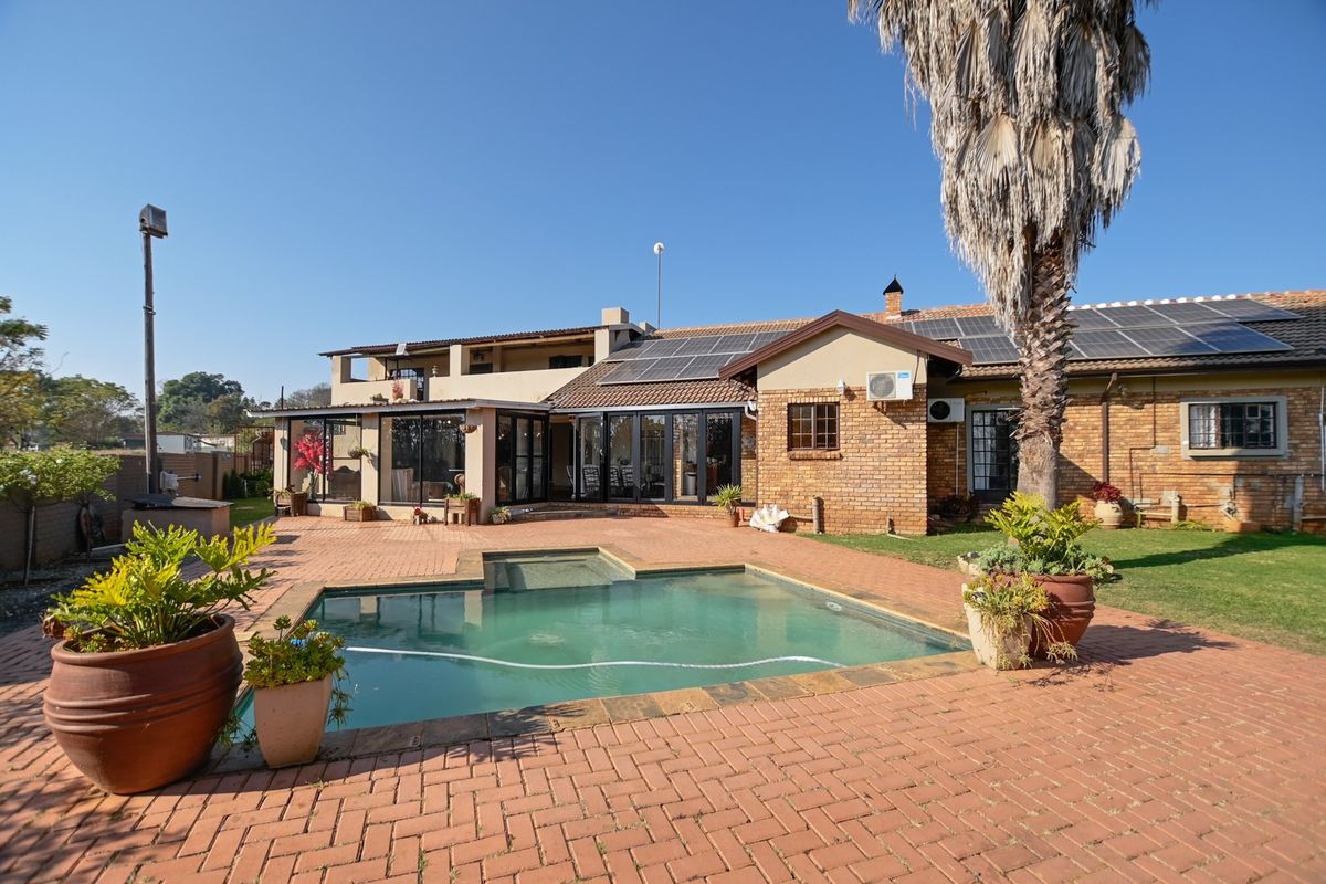 Rear exterior view featuring a swimming pool, brick paved patio, solar panels on the roof, and brick facade with large sliding doors.