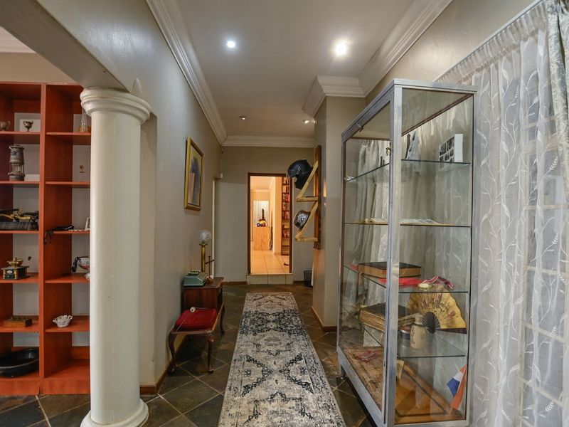 A well-lit hallway featuring tiled flooring, decorative cornicing, a structural column, and built-in shelving, leading towards an adjacent room.