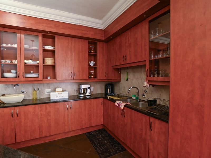 A functional kitchen featuring warm-toned wooden cabinetry, granite countertops, a double basin sink, and classic crown molding detailing.