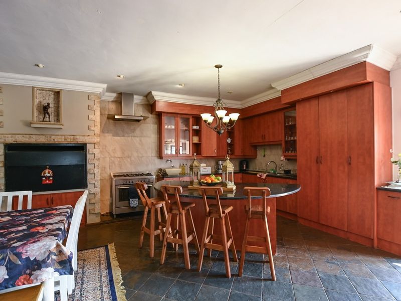 Spacious kitchen featuring dark wood cabinetry, granite countertops, a central island, and a built-in fireplace, finished with stone tile flooring.