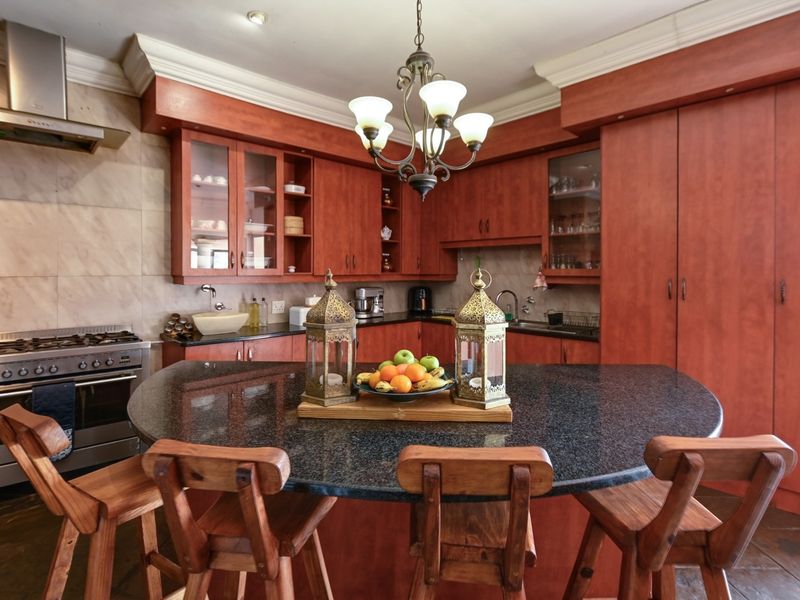 A spacious kitchen featuring warm-toned wooden cabinetry, granite countertops, a central island, and stainless steel appliances, including a gas stove and extractor fan.