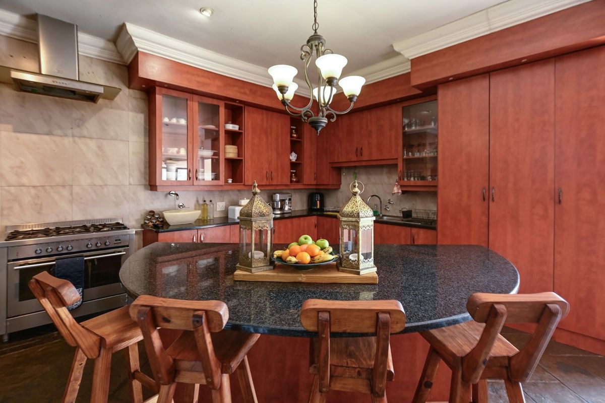 A spacious kitchen featuring warm-toned wooden cabinetry, granite countertops, a central island, and stainless steel appliances, including a gas stove and extractor fan.