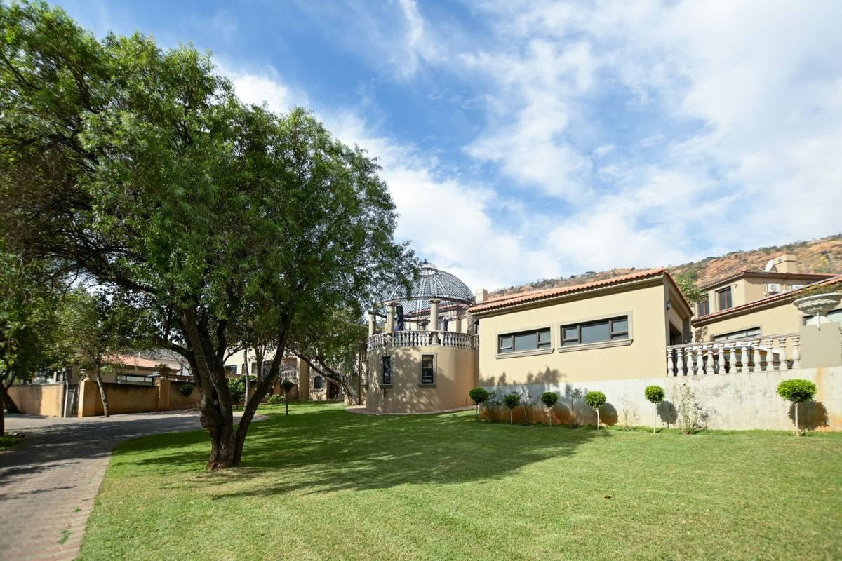 A spacious rear garden featuring a manicured lawn, mature trees, and a unique domed architectural structure with a terrace and balustrade.