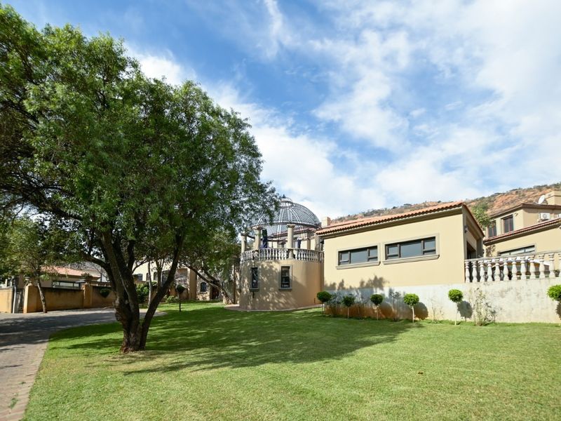 A spacious rear garden featuring a manicured lawn, mature trees, and a unique domed architectural structure with a terrace and balustrade.