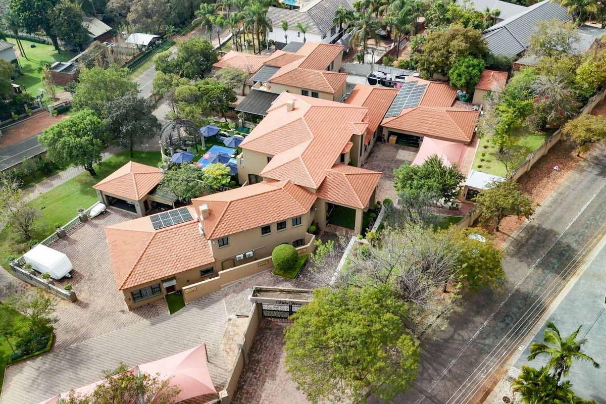 Aerial view of a large residential property featuring multiple roof sections, solar panels, extensive paved driveway, and established garden areas.