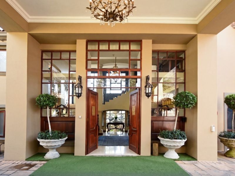 Grand entrance featuring double wooden doors, expansive glass paneling, and a covered portico with elegant lighting fixtures, providing a sophisticated welcome to the home.