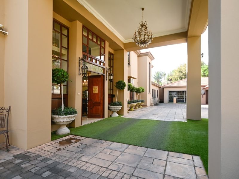 A grand covered entrance featuring a paved driveway, artificial turf, and elegant architectural pillars leading to a large timber front door.