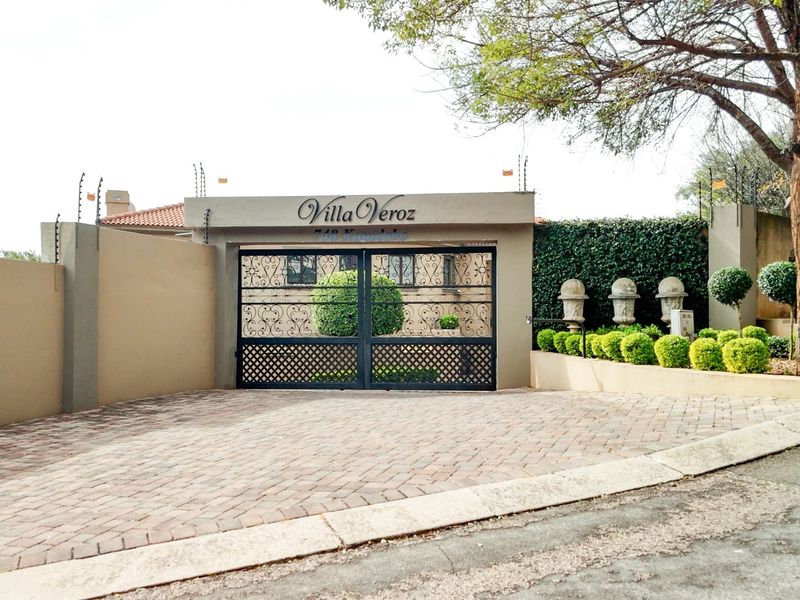 Front entrance view of the property featuring a paved driveway, secure wrought iron gate, and well-maintained boundary wall with electric fencing.
