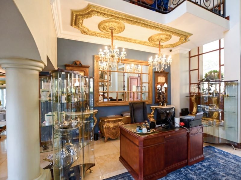A grand interior space featuring ornate gold ceiling detailing, tiled flooring, and a prominent staircase, currently utilized as a formal office or reception area.