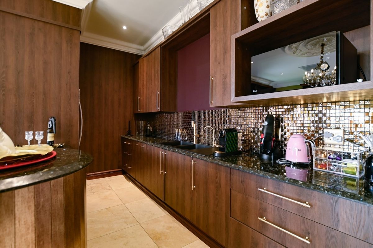 A well-appointed kitchen featuring dark wood cabinetry, granite countertops, a metallic mosaic backsplash, and stone flooring with integrated microwave and modern fixtures.