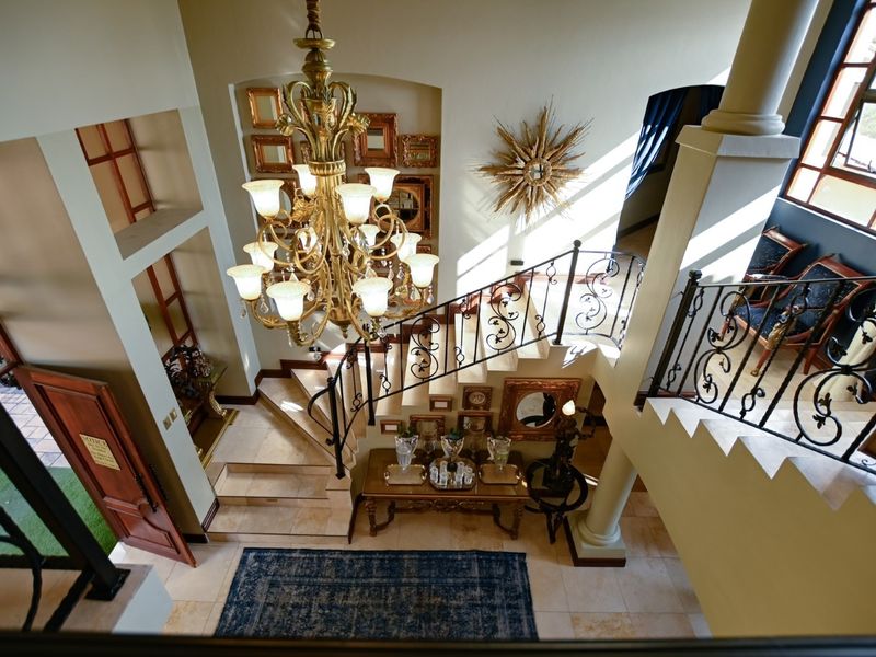 Grand entrance foyer featuring a sweeping staircase with wrought iron railings, stone tile flooring, and an impressive central chandelier.