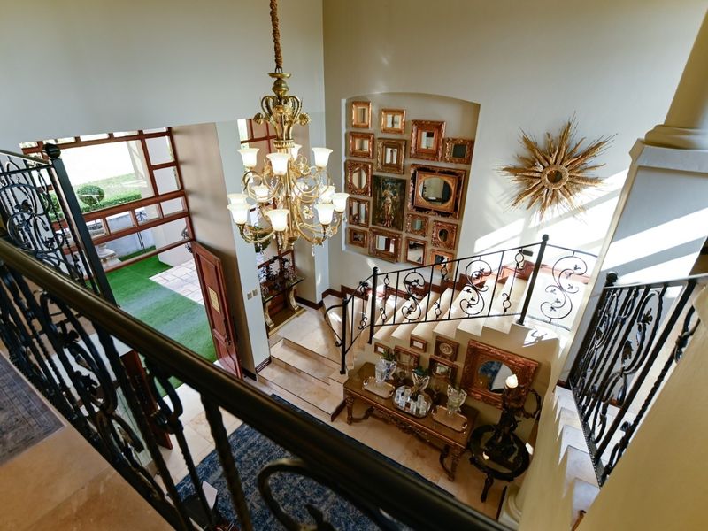 Grand double-volume entrance hall featuring a stone staircase, ornate wrought iron balustrades, and a prominent chandelier, creating an elegant and welcoming foyer.
