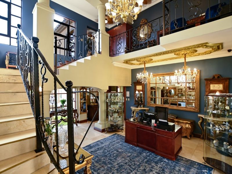 Grand double-volume entrance hall featuring a stone staircase with wrought iron railings, ornate ceiling details, and a mezzanine overlook.