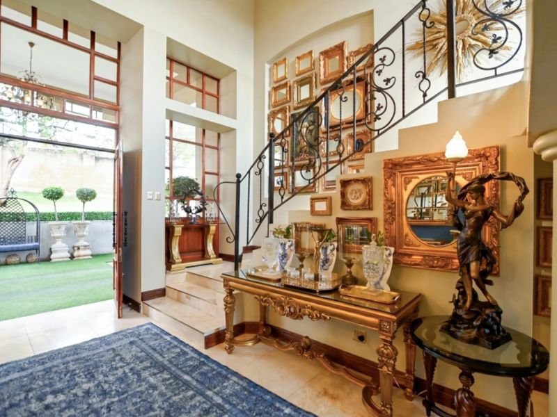 Grand entrance foyer featuring a decorative wrought iron staircase, high ceilings, and large glass windows providing natural light and views of the garden.