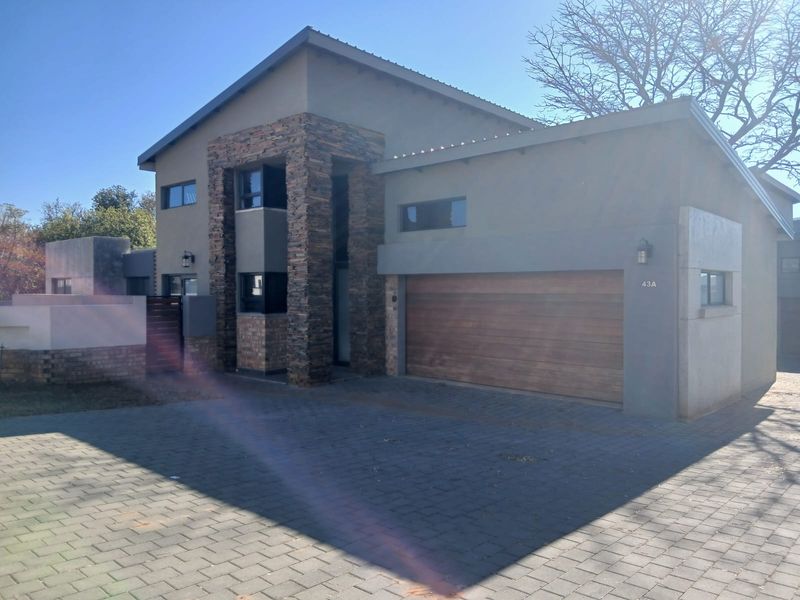 Front elevation of a modern duet property featuring stone cladding accents, a paved driveway, and a wooden automated garage door.