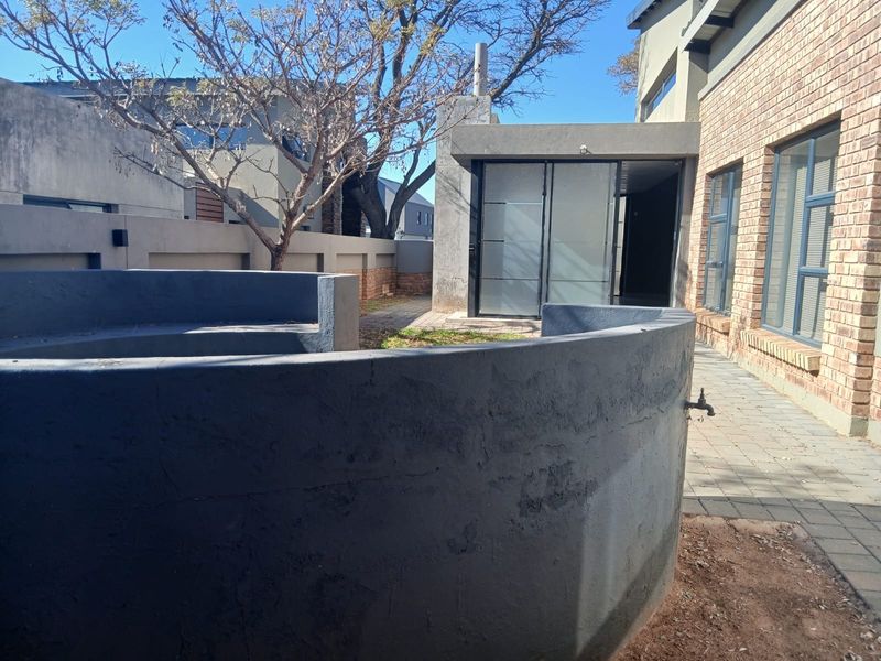 Rear exterior view of the duet property featuring a paved patio area, curved masonry wall, and access to the interior via sliding glass doors.