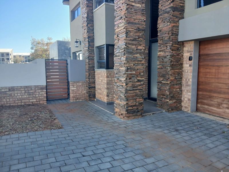 Front elevation of a modern duet property featuring stone-clad pillars, face brick accents, a paved driveway, and a wooden garage door.