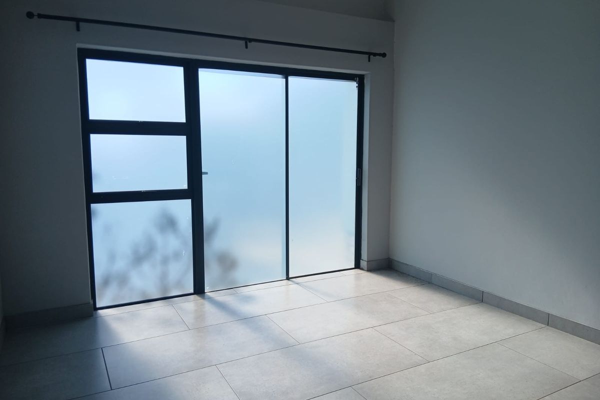 A bright, empty bedroom featuring modern large-format floor tiles and a large aluminium sliding door providing natural light.
