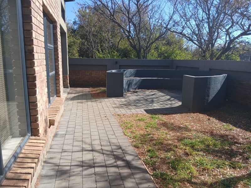 A private outdoor patio area featuring brick paving, a built-in concrete bench, and a surrounding boundary wall, offering a quiet space for relaxation.