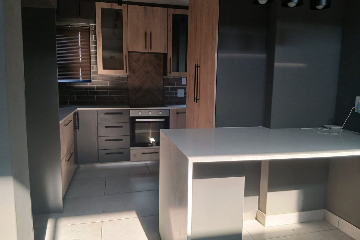 Modern kitchen featuring contemporary two-tone cabinetry, stone countertops, built-in oven, and stylish subway tile backsplash with integrated lighting.