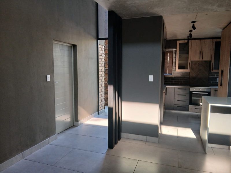 Modern open-plan kitchen featuring sleek cabinetry, built-in appliances, and a central island, complemented by contemporary tiled flooring and exposed concrete ceiling details.