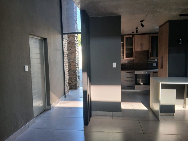 Modern open-plan living area featuring sleek cabinetry, a built-in oven, stone-clad architectural details, and large format floor tiles with contemporary track lighting.