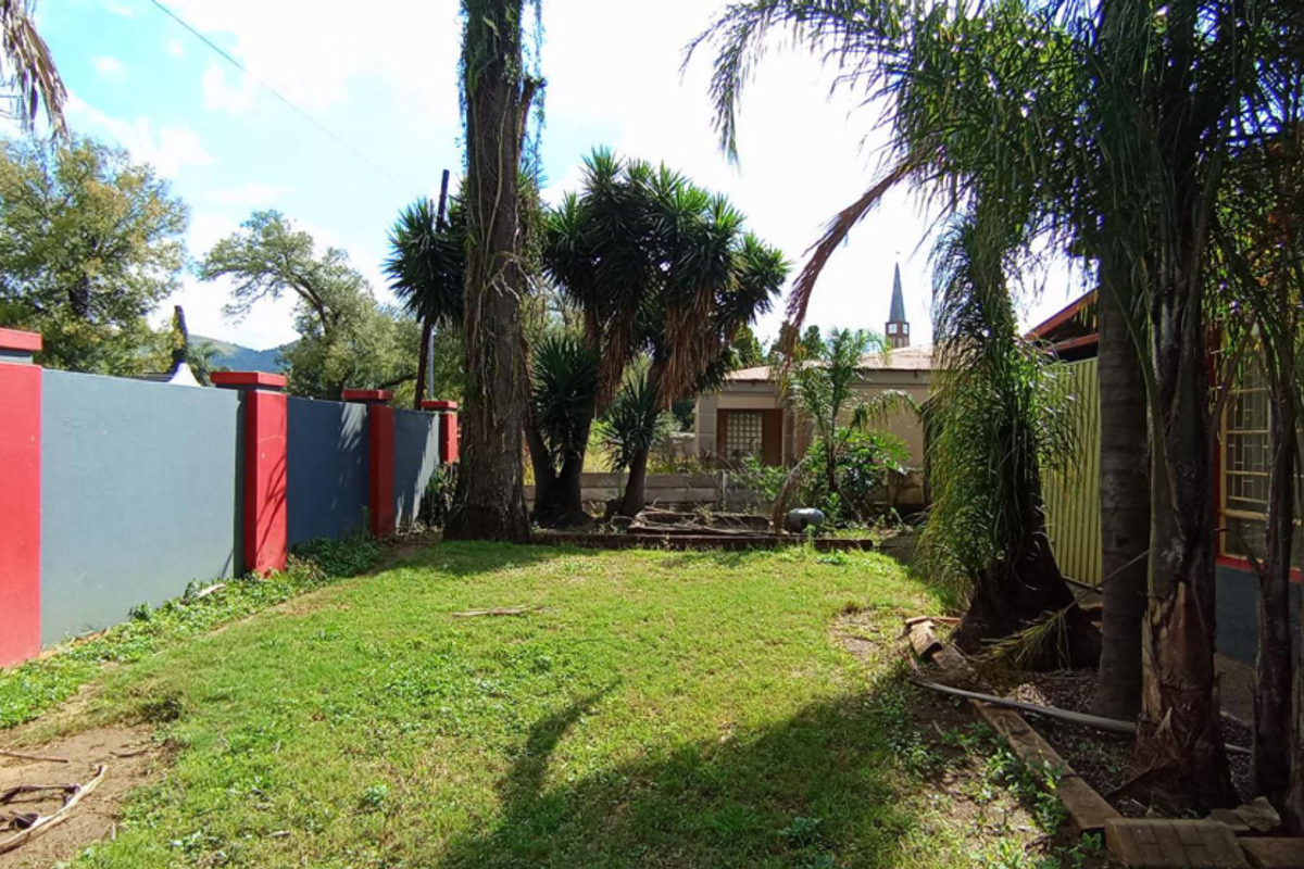 A rear garden area featuring a lawn, mature trees, and a painted boundary wall.