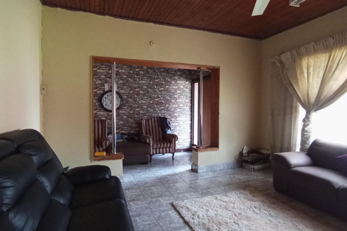 Living room featuring tiled flooring, a timber ceiling, and a decorative stone-effect accent wall with a large opening connecting to an adjacent space.