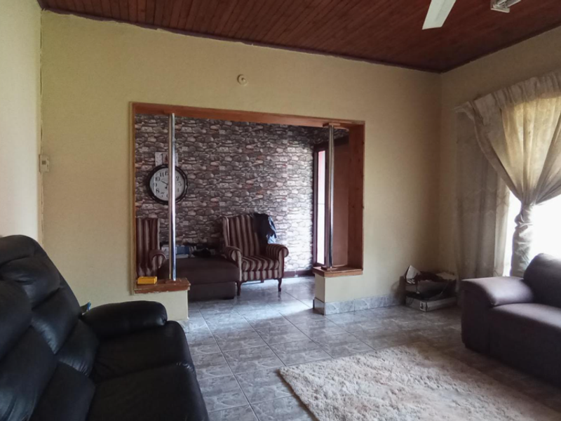 Living room featuring tiled flooring, a timber ceiling, and a decorative stone-effect accent wall with a large opening connecting to an adjacent space.