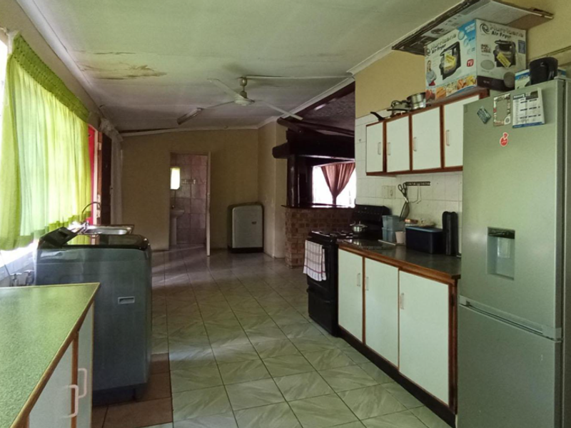 A dated kitchen featuring tiled flooring, built-in cabinetry, and a ceiling fan, showing signs of ceiling water damage and general wear.