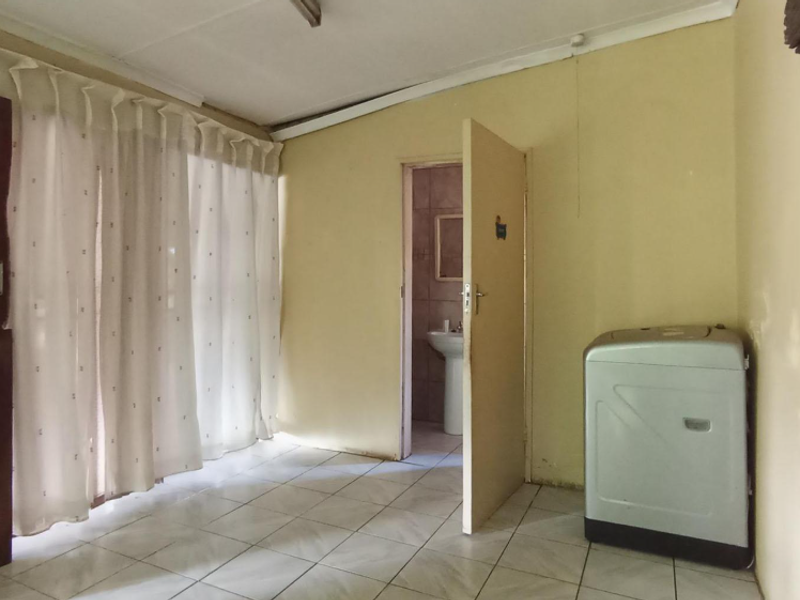 A simple bedroom featuring tiled flooring and an en-suite bathroom with a pedestal basin, offering a blank canvas for potential renovation and interior design updates.