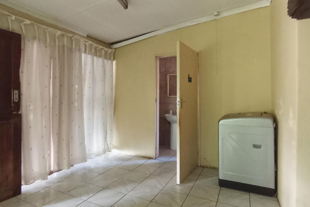 A simple bedroom featuring tiled flooring and an en-suite bathroom with a pedestal basin, offering a blank canvas for potential renovation and interior design updates.