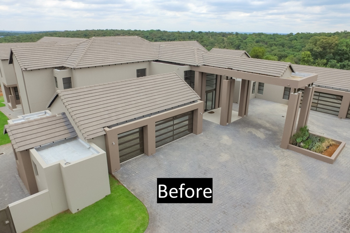 Aerial view of a modern luxury residence featuring a large paved driveway, multi-car garage, and expansive tiled roof structure set in a scenic landscape.
