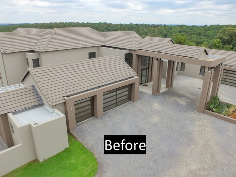 Aerial view of a modern luxury residence featuring a large paved driveway, multi-car garage, and expansive tiled roof structure set in a scenic landscape.
