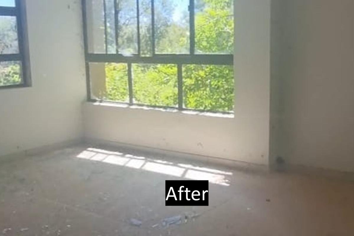 An empty bedroom featuring large windows with natural light, requiring significant renovation and flooring repairs to restore its condition.