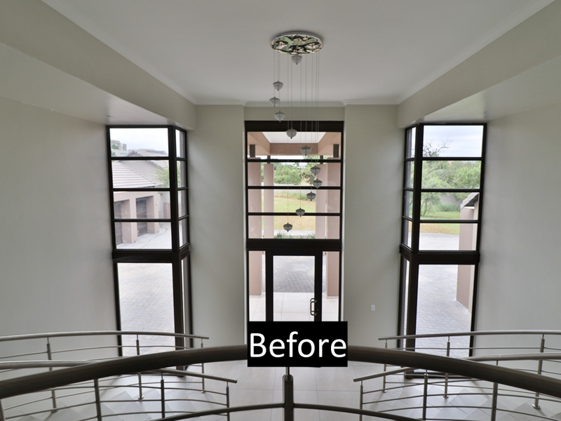 Spacious double-volume entrance hall featuring a grand staircase with metal balustrades, large glass windows, and a modern pendant light fixture.