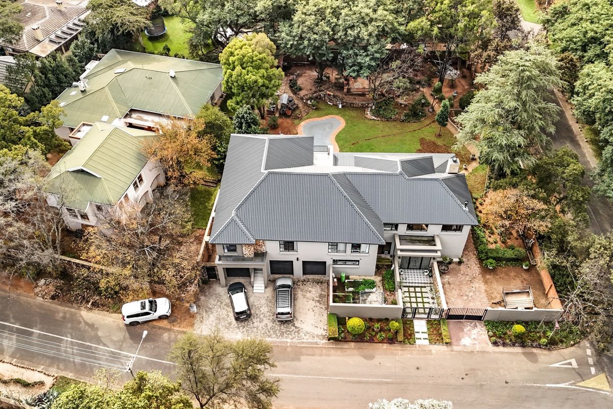 Aerial view of a modern residential property featuring a dark metal roof, paved driveway, double garage, and a well-maintained landscaped garden.