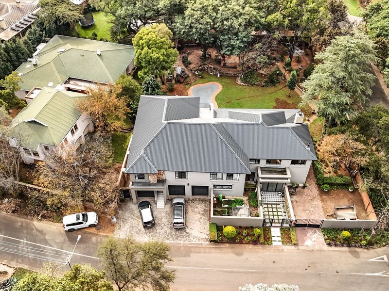 Aerial view of a modern residential property featuring a dark metal roof, paved driveway, double garage, and a well-maintained landscaped garden.