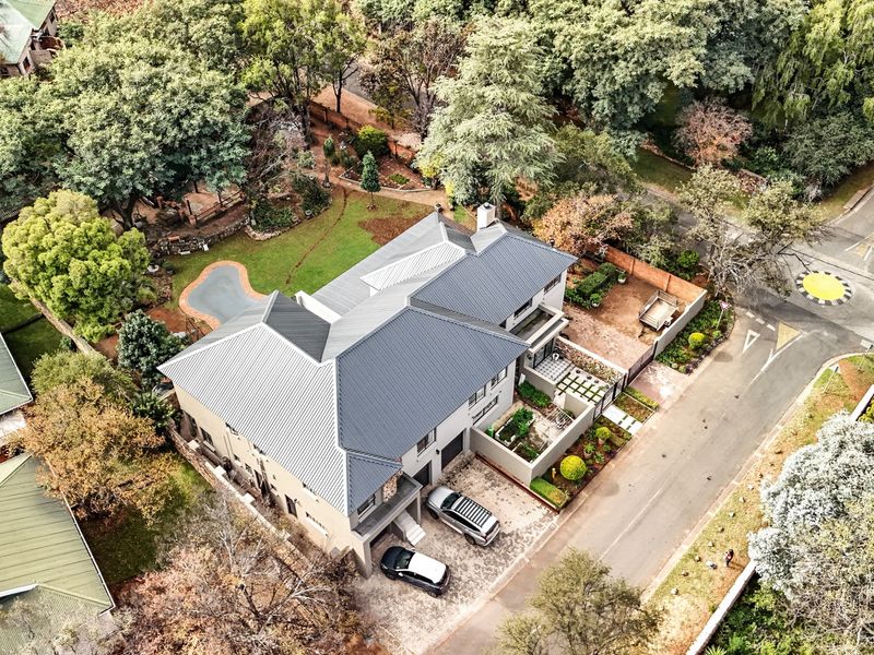 Aerial view of a residential property featuring a modern metal roof, paved driveway, swimming pool, and established garden in a suburban setting.