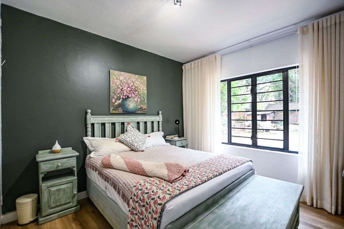 A well-maintained bedroom featuring dark accent wall, laminate flooring, and large metal-framed windows allowing natural light.