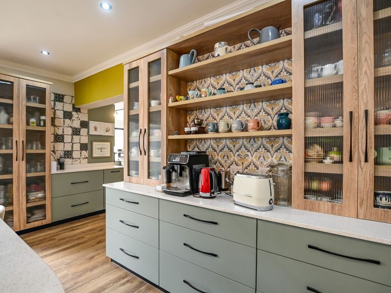 A modern, well-appointed kitchen featuring sage green cabinetry, quartz countertops, fluted glass display cabinets, and decorative patterned tile backsplash.