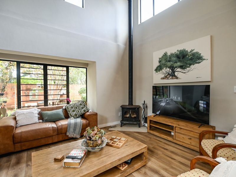 Spacious living room featuring a double-height ceiling, large windows with garden views, and a prominent freestanding wood-burning fireplace.