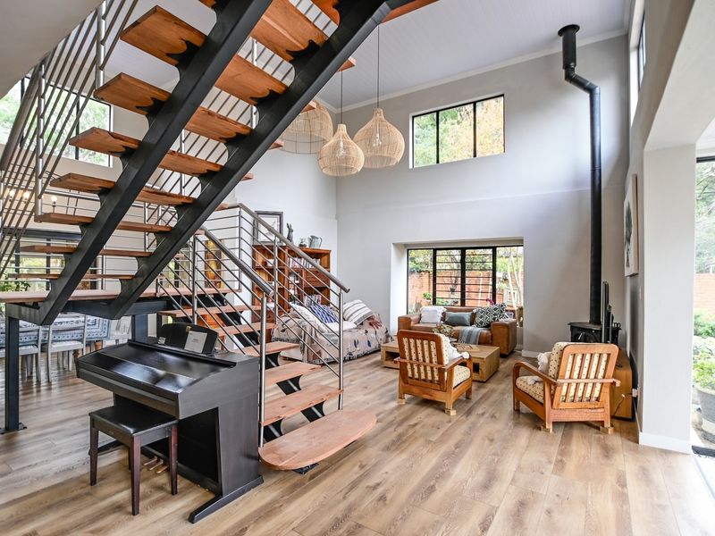 Spacious open-plan living area featuring a striking open-tread staircase, high ceilings, wood-burning fireplace, and large windows providing ample natural light.